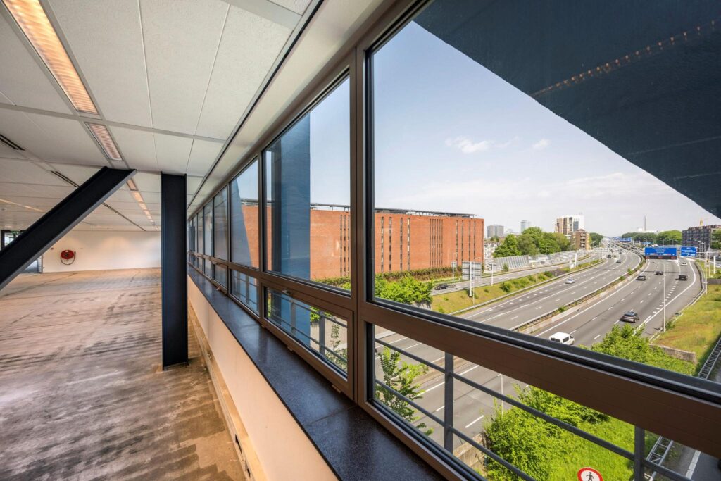 View from an empty office space at Bos en Lommerplein overlooking the highway and surrounding buildings.